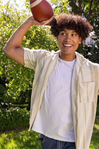 Hispanic Young Man Raising Football in Sunny Backyard Smiling and Preparing to Throw
