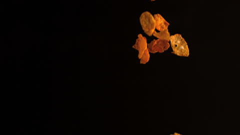Golden Cereal Flakes Falling Against Dark Background