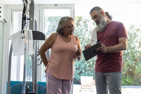 Senior woman receiving personal training guidance with tablet in home gym
