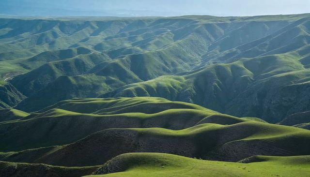 Sunlit rolling green hills and deep valleys on remote plateau with smooth ridgelines