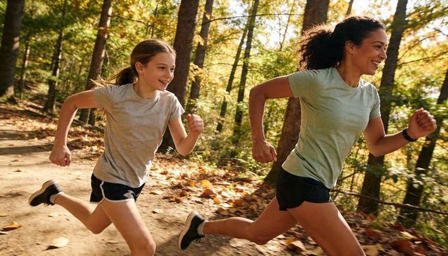 Adult and teen running on sunlit autumn forest trail