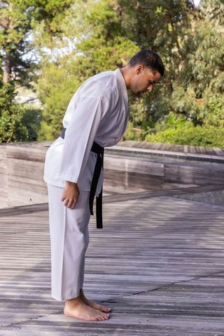 Man in white gi and black belt bowing outdoors with discipline