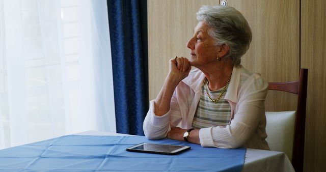 Thoughtful Elderly Woman Sitting by Window with Tablet - Download Free Stock Images Pikwizard.com