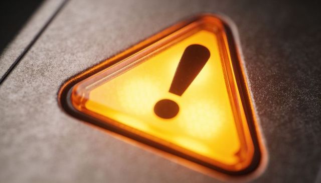 Amber triangular warning light closeup on metal control panel with exclamation mark