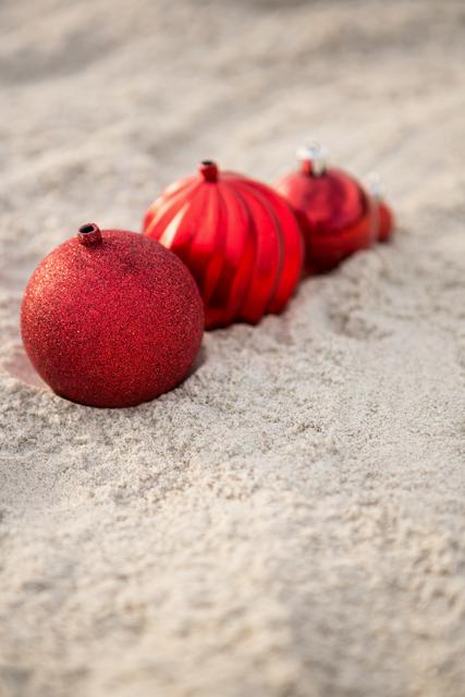 Red Christmas baubles arranged on sandy beach, creating a festive holiday atmosphere in a tropical or coastal setting. Ideal for use in holiday marketing materials, travel brochures, or social media posts promoting winter vacations in warm destinations. Perfect for illustrating unique holiday celebrations or Christmas in July themes.