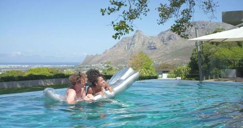 Couple floating on metallic pool float at infinity pool with mountain ocean view