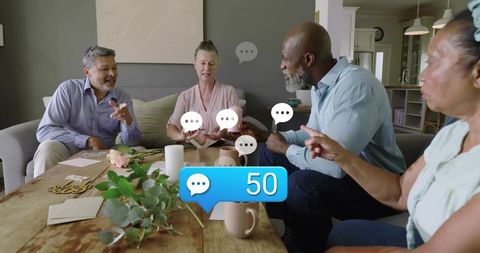 Mature friends chatting over cards at cozy living room table with 50 chat notifications