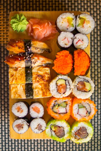 Top view of assorted sushi rolls including nigiri and maki arranged on a wooden board. Vivid colors of fish, vegetables, and roe make this perfect for scenes involving Japanese cuisine, fine dining, or restaurant menus.