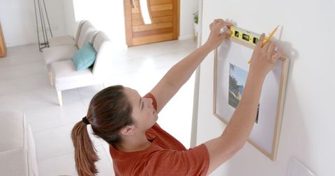Woman using spirit level hanging picture frame in living room