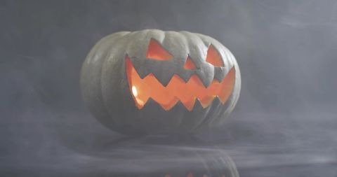 Glowing jack-o'-lantern floating on misty surface with amber candlelight and reflection
