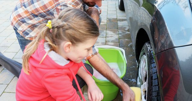 Happy caucasian father and daughter washing car in garden. Fatherhood, childhood, togetherness, transport and lifestyle, unaltered.