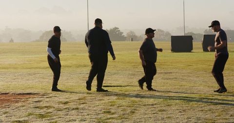 Mature male teammates walking across dewy sports field during morning training session