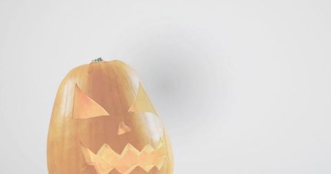 Carved halloween pumpkin lantern emitting warm amber glow on minimal white backdrop