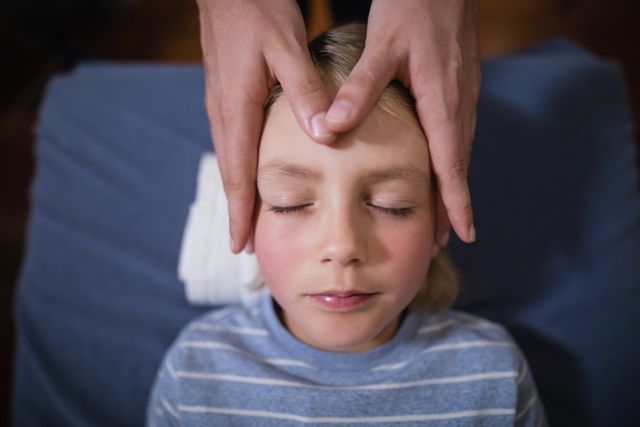 Boy receiving head massage from therapist in hospital. Ideal for use in articles about pediatric healthcare, wellness treatments for children, relaxation techniques, and therapeutic practices. Suitable for healthcare brochures, wellness blogs, and educational materials on child therapy.