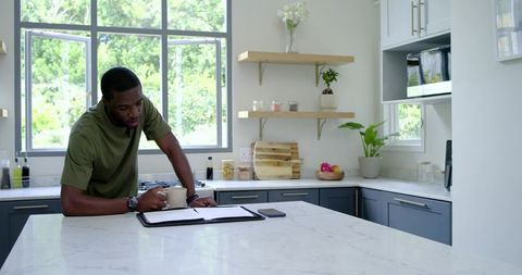 African american man reviewing papers on modern marble kitchen island while holding coffee