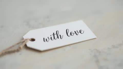 Macro video focusing on white gift tag reading 'with love' calligraphy on pale tabletop