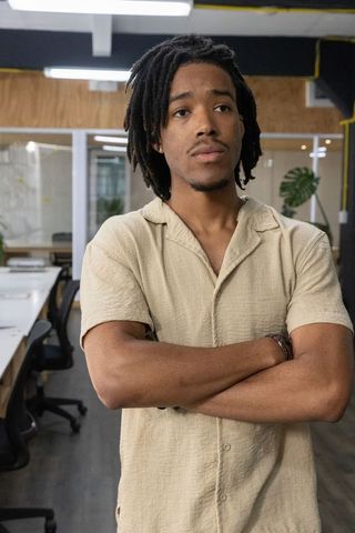 Confident coworking professional with dreadlocks standing arms crossed in modern office