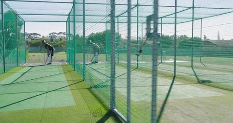Male cricketers practicing batting in outdoor net cages on sunny training ground