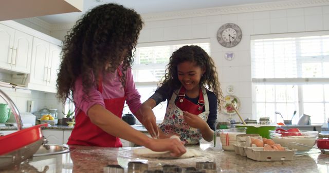 Two African American girls, wearing aprons, enjoying baking together in a bright and clean kitchen. Perfect for concepts such as family bonding, childhood activities, domestic life, playful learning, and cooking at home.
