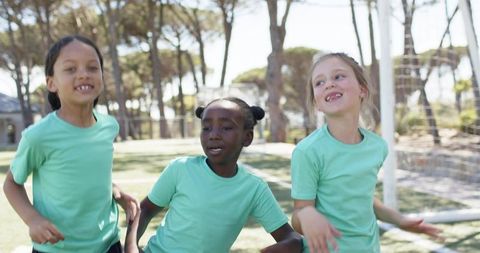 Smiling multiracial girls celebrating at school soccer field wearing matching mint shirts