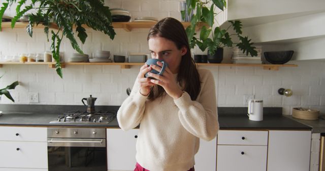 Caucasian non-binary transgender woman drinking coffee in kitchen. spending quality time at home alone, body inclusivity.