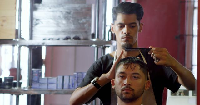 A young Latino barber is styling the hair of a Caucasian male client in a barbershop, with copy space. Precision and care are evident as the barber works to create a trendy hairstyle.