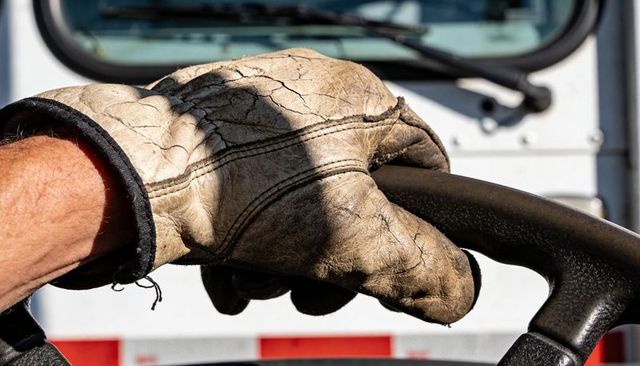 Worn leather glove gripping steering wheel in truck cab close-up of trucker driving long-haul