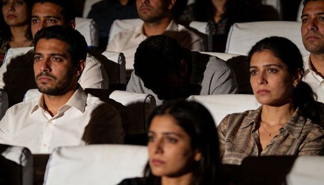 South asian adults watching lowlight film screening in theater with white headrests
