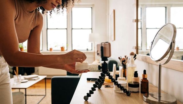 Curly-haired creator filming skincare tutorial on vanity with smartphone tripod
