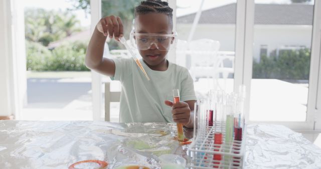 Young boy wearing safety goggles conducting a science experiment at home using test tubes. Great for educational platforms, children's learning activities, science-related articles, or homeschooling resources.