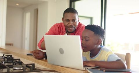 Father helping son with laptop at kitchen counter working homework and learning technology