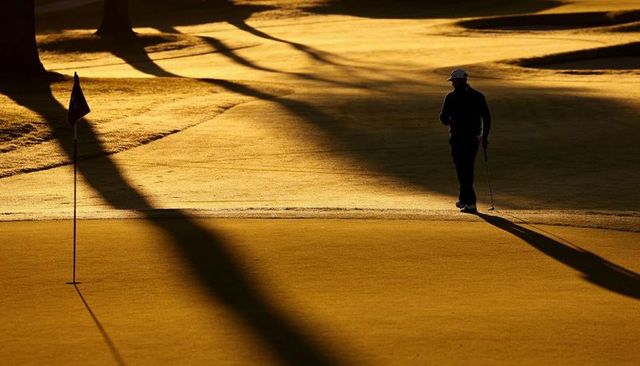 Solitary golfer walking on golden putting green at sunrise casting dramatic long shadows