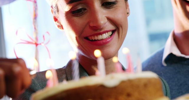 Happy moment of a young woman joyfully celebrating her birthday with a cake lit with candles. Suitable for use in blog posts about birthday celebrations, party planning ideas, or emotional moments shared with loved ones.