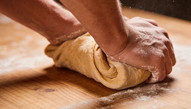 Artisanal baker kneading and folding rustic dough on floured wooden worktop closeup
