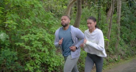 Couple jogging side-by-side on wooded paved trail for outdoor fitness and wellness