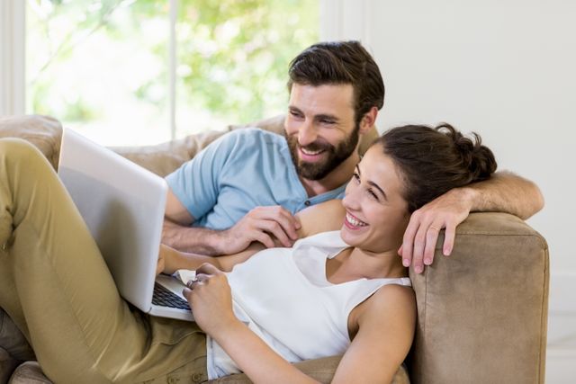 Happy couple lying on sofa and using laptop at home
