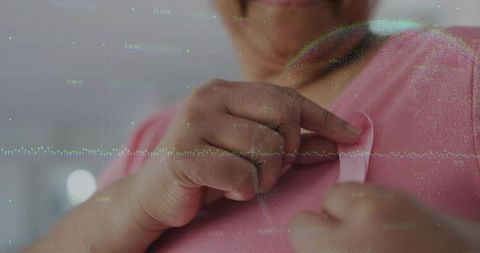 Senior woman pinning pink ribbon on chest for breast cancer awareness with data overlay