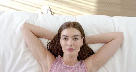 Woman reclining on bed under sunlit blinds enjoying relaxed morning