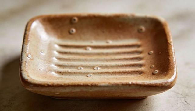 Handmade ceramic soap dish resting on marble countertop with water droplets macro close-up