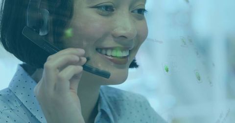 Smiling asian customer support agent wearing headset and viewing translucent screen