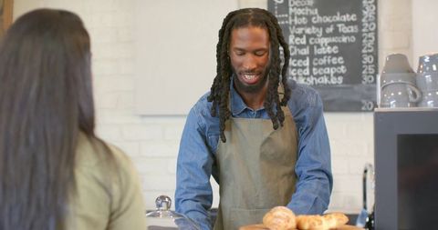 Friendly african american barista serving indian customer at coffee shop with pastries