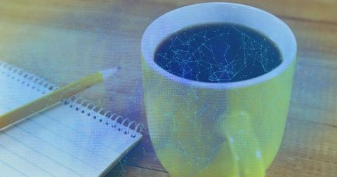 Yellow coffee mug sitting on wooden desk with notebook and blue digital network overlay