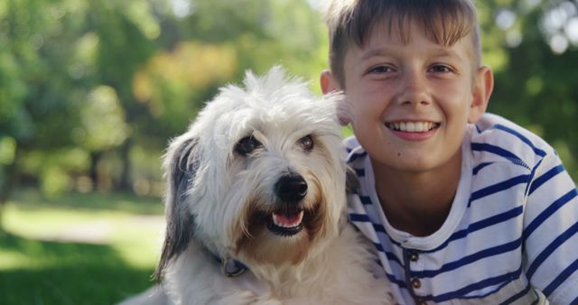 Young boy enjoying sunny day at park with fluffy white dog, making it perfect for illustrating concepts of companionship, happiness, and outdoor activities. Ideal for use in promotional materials for pet products, family time advertisements, or outdoor activity campaigns.