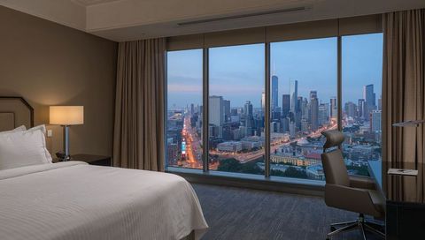 Luxury hotel guestroom with floor-to-ceiling window overlooking urban skyline at twilight