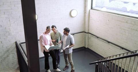 Collaborative coworkers reviewing plans in modern office stairwell
