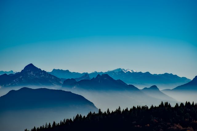 Panoramic view of distant mountain range with morning haze under clear blue sky. Perfect for travel websites, nature blogs, and outdoor adventure promotions. Ideal for use in posters, postcards, or background images to evoke a sense of tranquility and natural beauty.