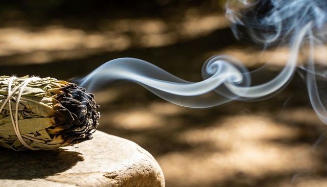 Smudging sage bundle releasing curling smoke on rustic stone for ritual cleansing