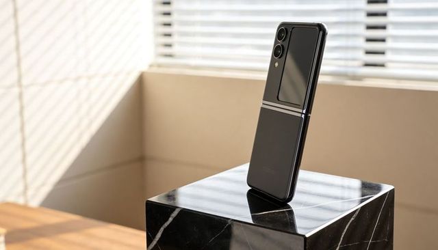 Glossy black foldable smartphone standing on marble pedestal with dual cameras and hinge