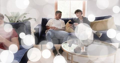 Two friends relaxing on sofa sharing smartphone and drink in bright modern living room