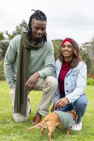 Kneeling in park petting small dog, diverse couple sharing casual affection in greenspace